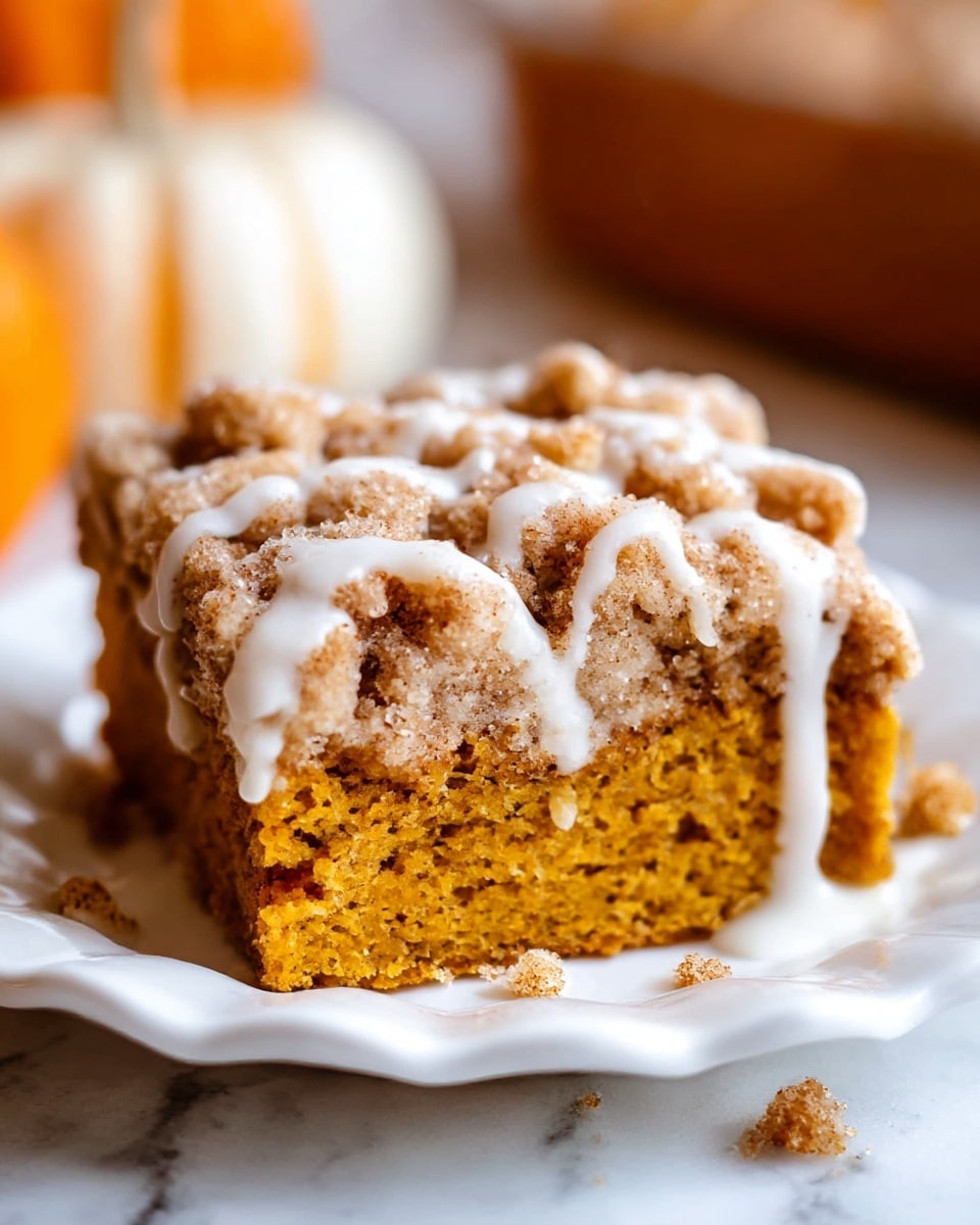 A close-up view of a two-layer dessert on a white scalloped plate, placed on a white marbled surface; the bottom layer is moist and dense with a warm pumpkin orange color, while the top layer is a thick, crumbly streusel with a golden brown texture sprinkled with sugar, and white glaze drizzled unevenly on top and slightly spilling onto the plate, with some crumbs scattered around the base; soft focus pumpkins are visible in the blurred background. photo taken with an iphone --ar 4:5 --v 7