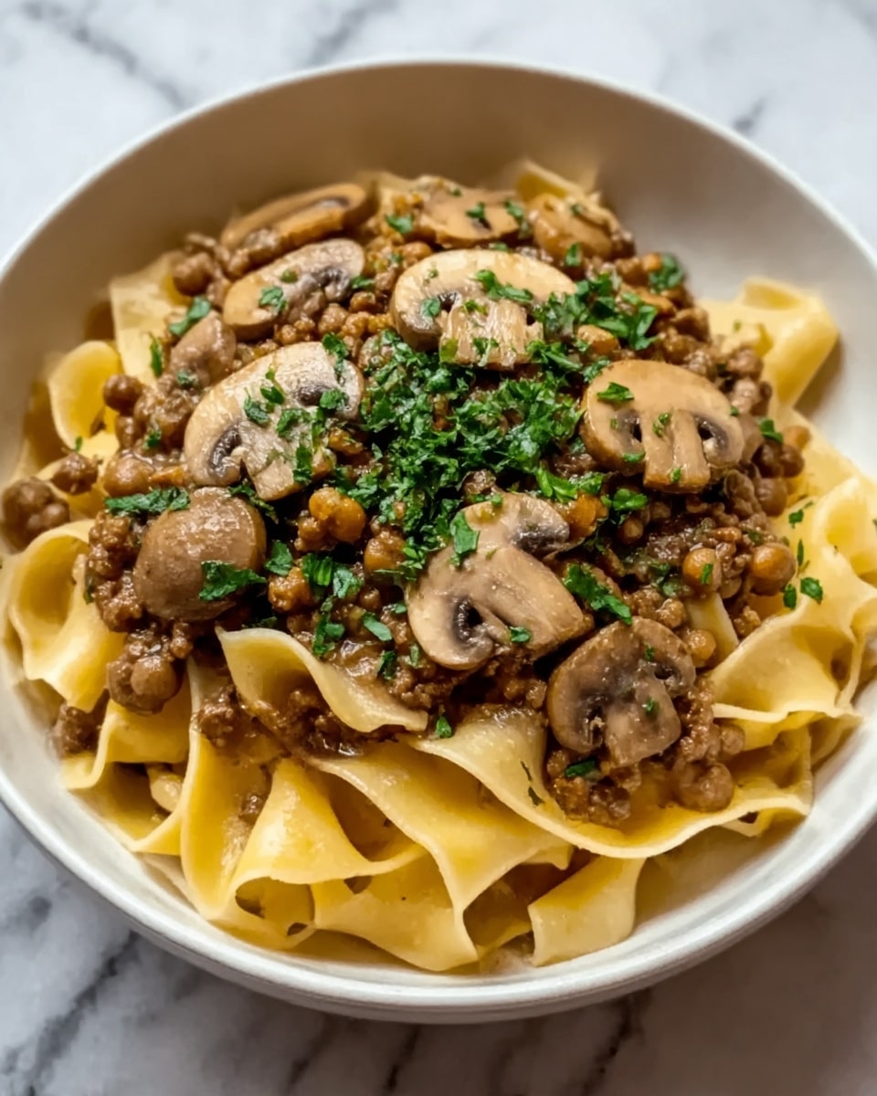 A white bowl filled with wide, flat pasta noodles at the bottom layer, topped with a generous portion of rich brown sauce with ground meat mixed in. On top of the sauce, there are several cooked brown mushroom slices evenly spread out. The dish is finished with chopped green herbs sprinkled over the mushrooms, adding a fresh touch to the colors. The bowl sits on a white marbled surface. photo taken with an iphone --ar 4:5 --v 7