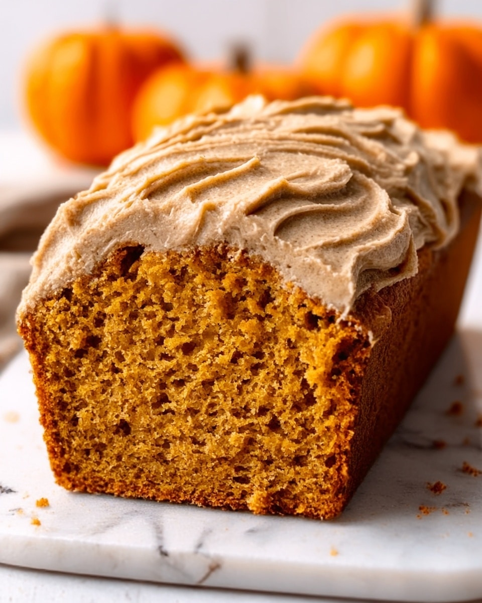The image shows a loaf of orange-colored cake sliced to reveal its soft and moist inside texture. The top layer is covered with a thick, light brown frosting that looks slightly crumbly and textured, with some frosting flowing over the edges on both sides. The cake is placed on a white marbled surface with blurred orange fruits in the background, adding a warm and fresh feeling to the scene. Photo taken with an iphone --ar 4:5 --v 7