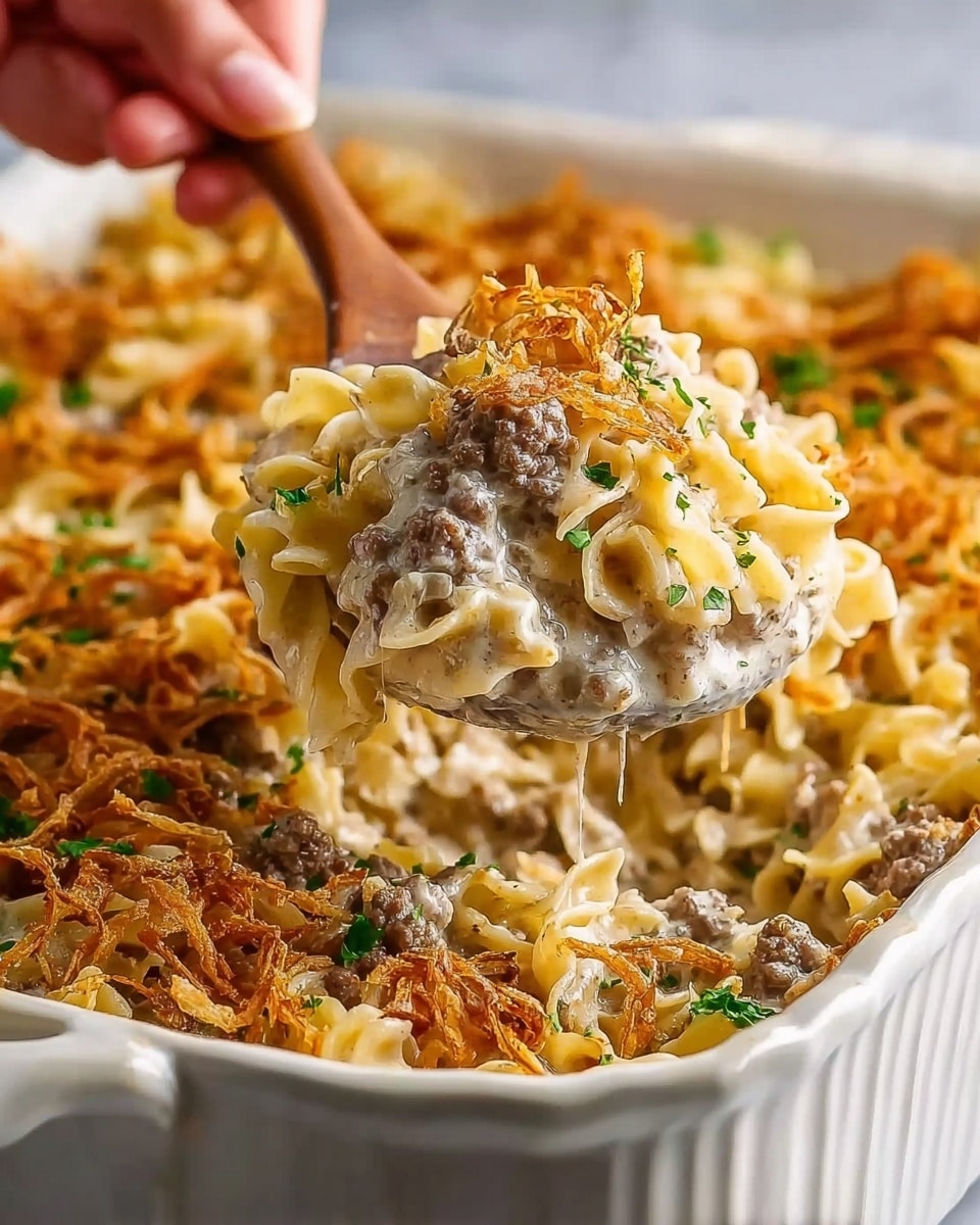 The image shows a close-up of a white ceramic baking dish filled with a layered casserole. The bottom layer consists of a creamy, pale sauce mixed with browned ground meat chunks, topped with curly, pale yellow egg noodles. Scattered thin, crispy golden-brown fried onions cover the top layer, adding texture, along with small pieces of fresh green parsley sprinkled for color. A wooden spoon held by a woman's hand scoops out a large portion of the casserole from the dish, revealing the mix of creamy, meaty, and crispy ingredients inside. The dish sits on a white marbled textured surface, creating a clean and bright background. Photo taken with an iphone --ar 4:5 --v 7