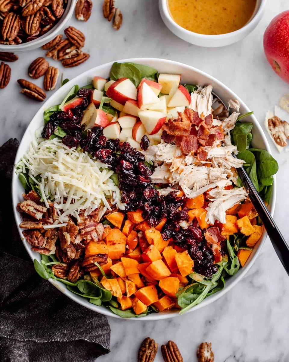 A large white bowl sits on a white marbled surface filled with a colorful salad arranged in separate layers and sections. At the base, there is a mix of leafy greens. On top, the ingredients are lined up in rows starting from the left with crunchy pecan halves in dark brown, followed by small cubes of red and white apple, crispy cooked bacon strips in dark reddish-brown, shredded white chicken breast pieces in the center, dark dried cranberries next to the chicken, and bright orange roasted sweet potato cubes on the right side. There are also thin, white cheese shavings layered near the pecans and sweet potatoes. A black spoon rests inside the bowl on the left edge. In the background, a small white bowl holds orange salad dressing next to a whole apple. photo taken with an iphone --ar 4:5 --v 7