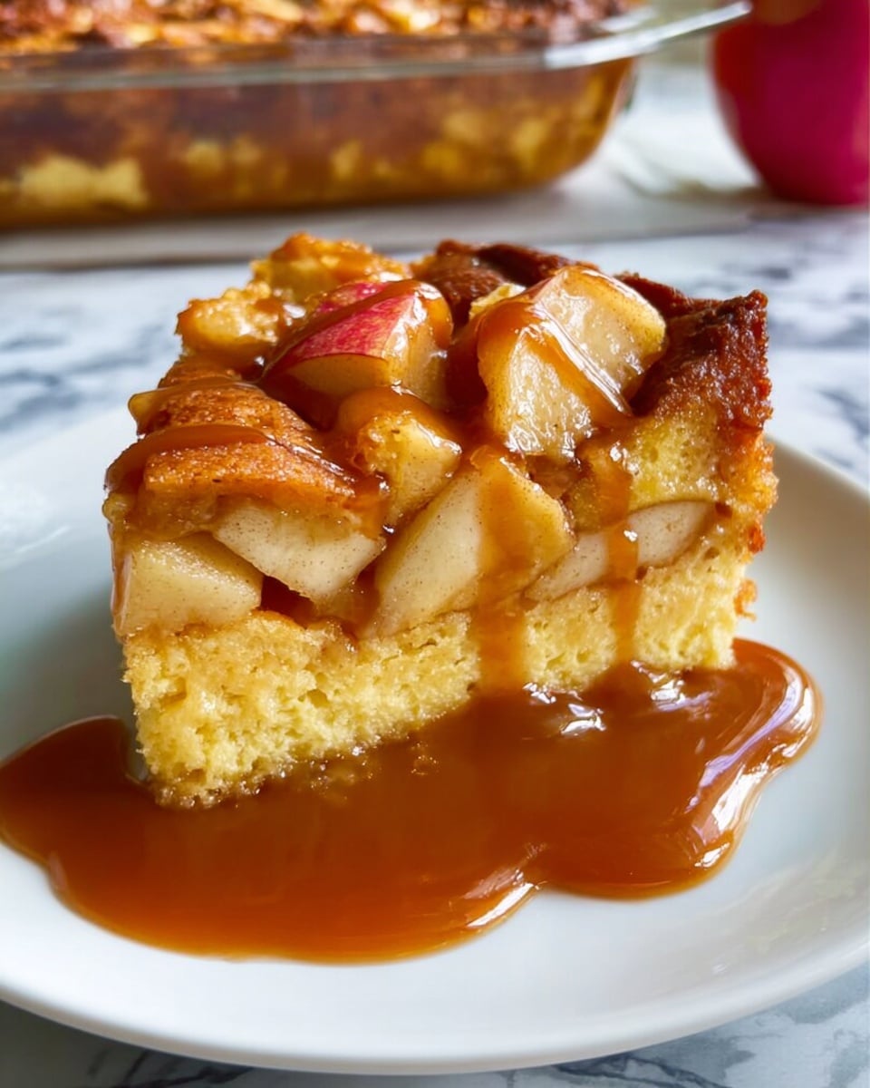 A close-up slice of baked dessert on a white plate sits on a white marbled surface. The slice has two main layers: the bottom layer is a soft, yellow cake with a slightly uneven texture, and the top layer is filled with chunks of cooked apples that have a light brown color and tender look. The dessert is topped with a shiny, thick caramel sauce that drips over the sides, adding a rich, glossy brown contrast to the light cake and fruit layers. Photo taken with an iphone --ar 4:5 --v 7