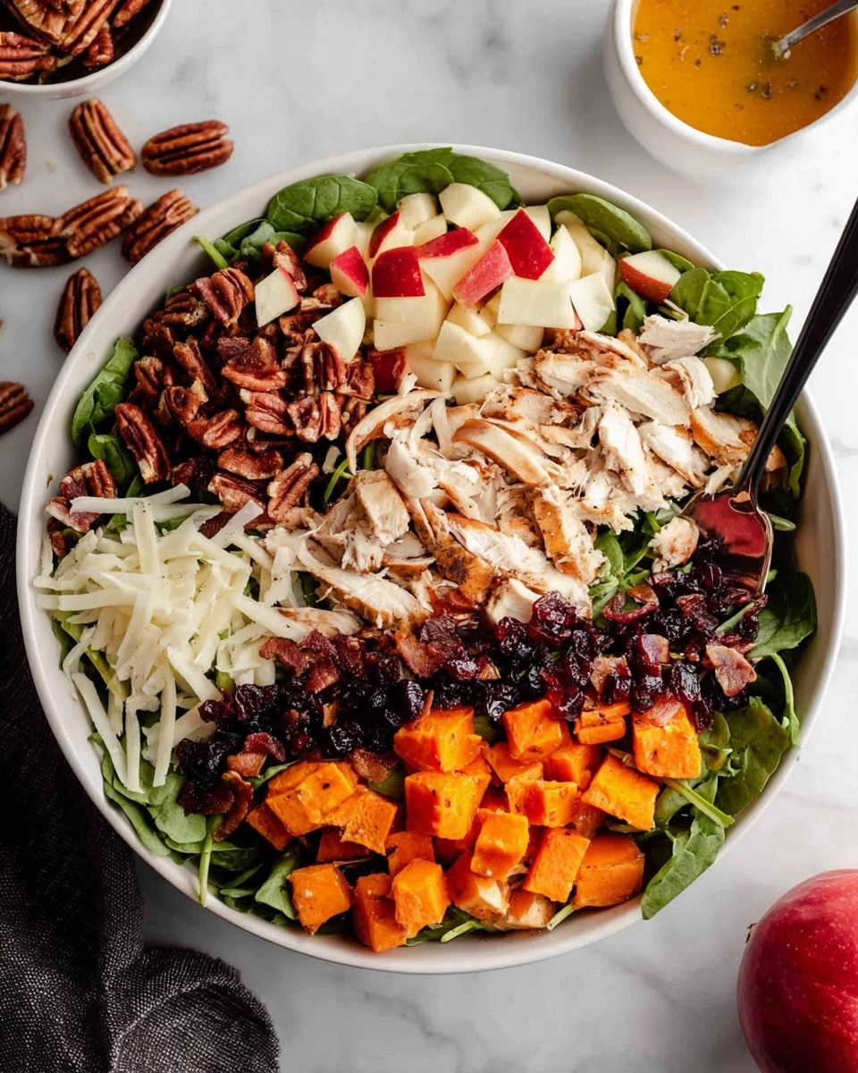A white bowl filled with a colorful salad arranged in neat layers on a white marbled surface; starting from the top left, there are dark brown pecans, followed by white shaved cheese, then small cubes of red-skinned apples, a layer of crispy brown bacon pieces, shredded white chicken placed in the center, a line of dark dried berries next to the chicken, and bright orange roasted sweet potato chunks at the bottom; underneath all these toppings is a bed of fresh green leafy spinach; a black spoon rests inside the bowl on the left side, some pecans are scattered outside the bowl, and a small white bowl with orange dressing and a whole red apple are near the top right corner. photo taken with an iphone --ar 4:5 --v 7