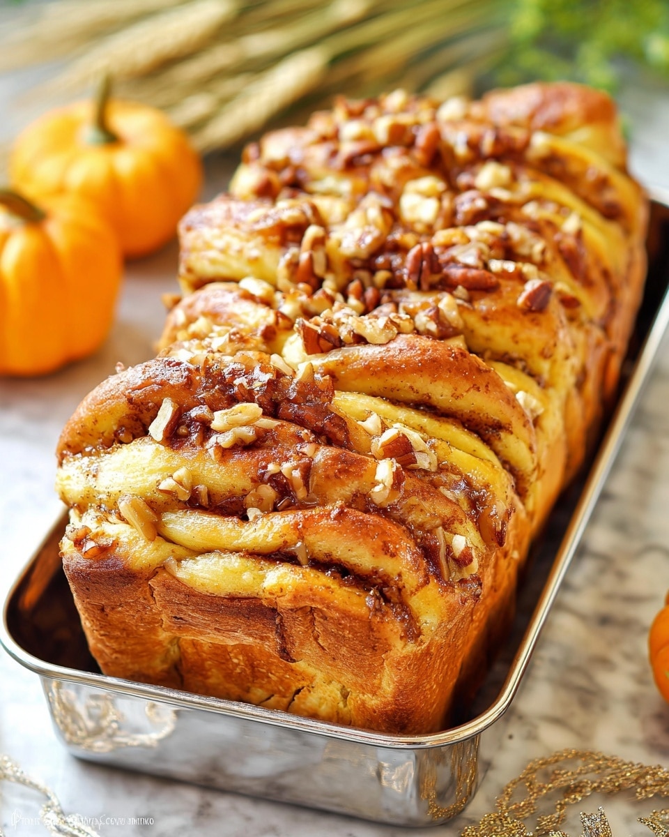 A loaf of pull-apart bread with a golden brown top and soft, fluffy layers twisted together, each layer showing a mix of light yellow dough and darker brown sweet filling, sprinkled generously with chopped nuts that add a crunchy texture on top and between the layers. The bread sits in a shiny silver tray that reflects the warm tones of the bread, placed on a white marbled texture surface with some small orange pumpkins and light green wheat stalks blurred in the background. photo taken with an iphone --ar 4:5 --v 7