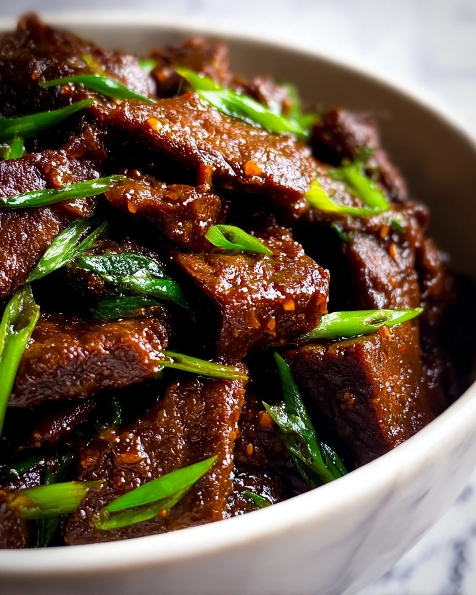 A close-up view of a dish consisting of multiple pieces of dark brown glazed beef, cooked with a shiny, sticky texture. The beef pieces are uneven and layered inside a white bowl, mixed with bright green slices of what looks like spring onions scattered throughout. The edges of the beef are slightly crispy, while the inside appears tender. The green onions add a fresh contrast to the rich brown meat. The background is a blurred white marbled texture. photo taken with an iphone --ar 4:5 --v 7