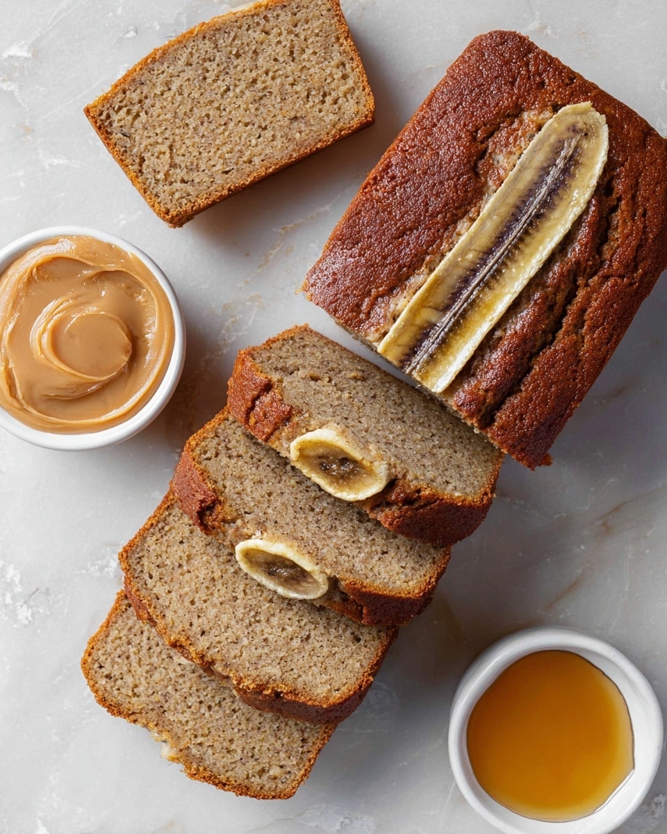 A sliced banana bread loaf is shown on a white marbled surface, with a brown crust on top and soft light brown crumb inside. There are three slices: two lie flat on the surface with visible banana pieces inside, and one slice stands upright showing a neat cross-section. The middle loaf section is cut into three parts with banana peel strips on top, displaying a layered texture of the bread and banana. To the left, there is a small white bowl of smooth light brown spread with a glossy finish, and below it, another small white bowl holds thick, shiny golden syrup. The overall look is warm and rustic. Photo taken with an iphone --ar 4:5 --v 7