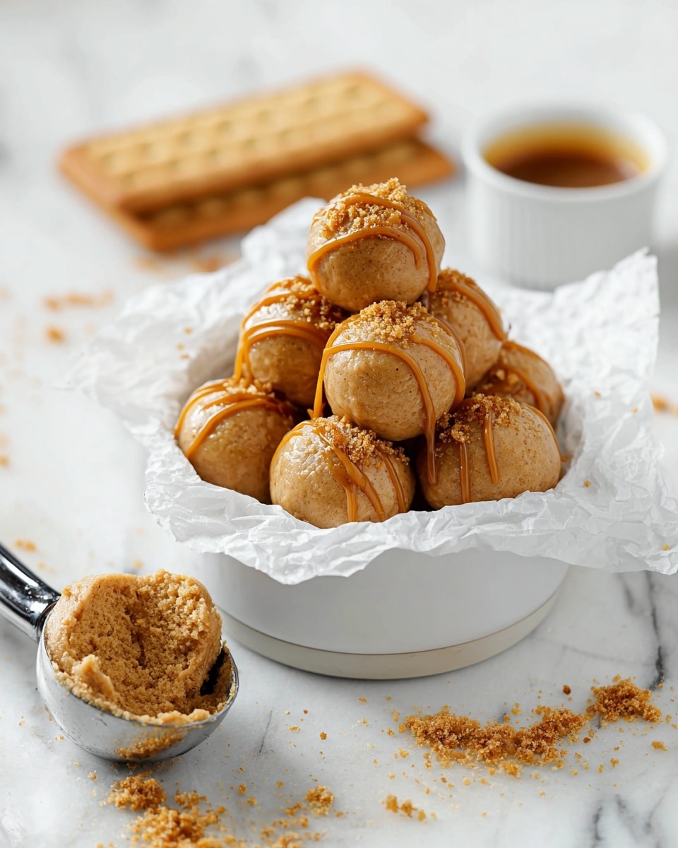 A white bowl lined with crumpled white parchment paper holds a stack of round, light brown balls with a smooth texture, each drizzled with caramel-colored syrup and sprinkled with crumbly biscuit crumbs on top. In the background, two rectangular biscuits lay flat on the white marbled surface, and a small white cup filled with caramel sauce sits blurred. In the foreground, a metal ice cream scoop with a chunk of the light brown mixture rests on the white marbled surface, with some crumbs scattered around. Photo taken with an iphone --ar 4:5 --v 7