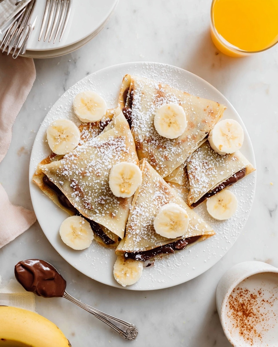 A white plate holds four folded crepes arranged diagonally, each with a thin, light beige outer layer. Between the folds is a dark chocolate spread layer, smooth and glossy. On top, there are several thin slices of banana scattered across the crepes and the plate. A dusting of white powdered sugar covers parts of the crepes, adding texture and a slight sparkle. To the side on the white marbled surface, there is a vintage silver spoon with chocolate spread, some banana slices, and a banana peel at the bottom left. Surrounding the plate, there are a small stack of white plates with two forks on the top left, a glass of orange juice at the top right, and a white cup with a drink sprinkled with cinnamon to the far right. photo taken with an iphone --ar 4:5 --v 7