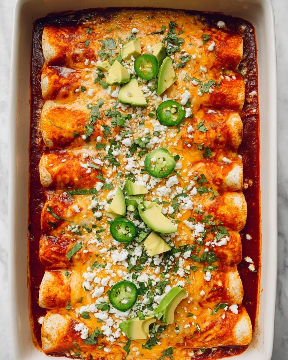 The image shows a white baking dish filled with eight rolled enchiladas arranged in two rows of four, covered with rich red sauce visible around and partially on the enchiladas. The enchiladas are topped with melted light yellow cheese, sprinkled with small white cheese crumbles, and fresh green chopped herbs scattered across the surface. Slices of green jalapeño peppers and avocado wedges are placed on top as garnish, adding fresh color contrast. The white marbled texture under the dish completes the setting. photo taken with an iphone --ar 4:5 --v 7