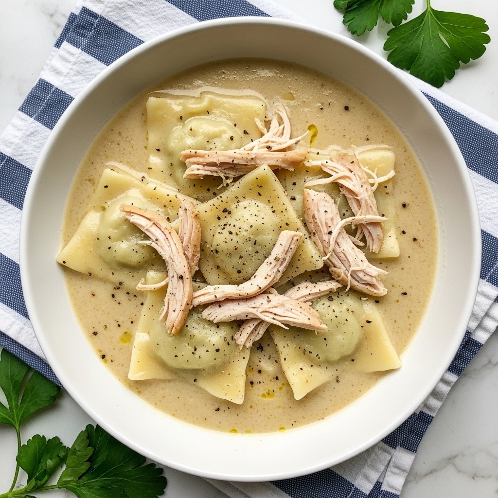 A white bowl filled with a creamy light beige soup with visible black pepper specks on top. Inside the soup, there are several square-shaped, soft-looking dumplings layered throughout. Shredded pieces of light brown chicken are scattered on and around the dumplings, partially submerged in the soup. The bowl is placed on a blue and white striped cloth, all set on a white marbled surface with some green leafy herbs around. photo taken with an iphone --ar 4:5 --v 7